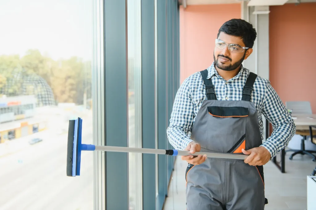 Window cleaner in overalls and safety glasses using a squeegee on floor-to-ceiling glass at a hospitality venue